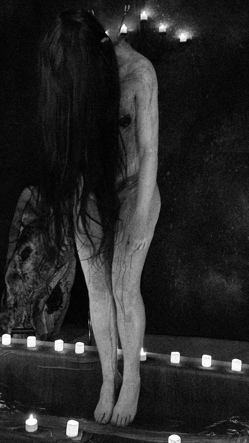 Black-and-white behind-the-scenes photograph of a performer in the candlelit BATHORY set